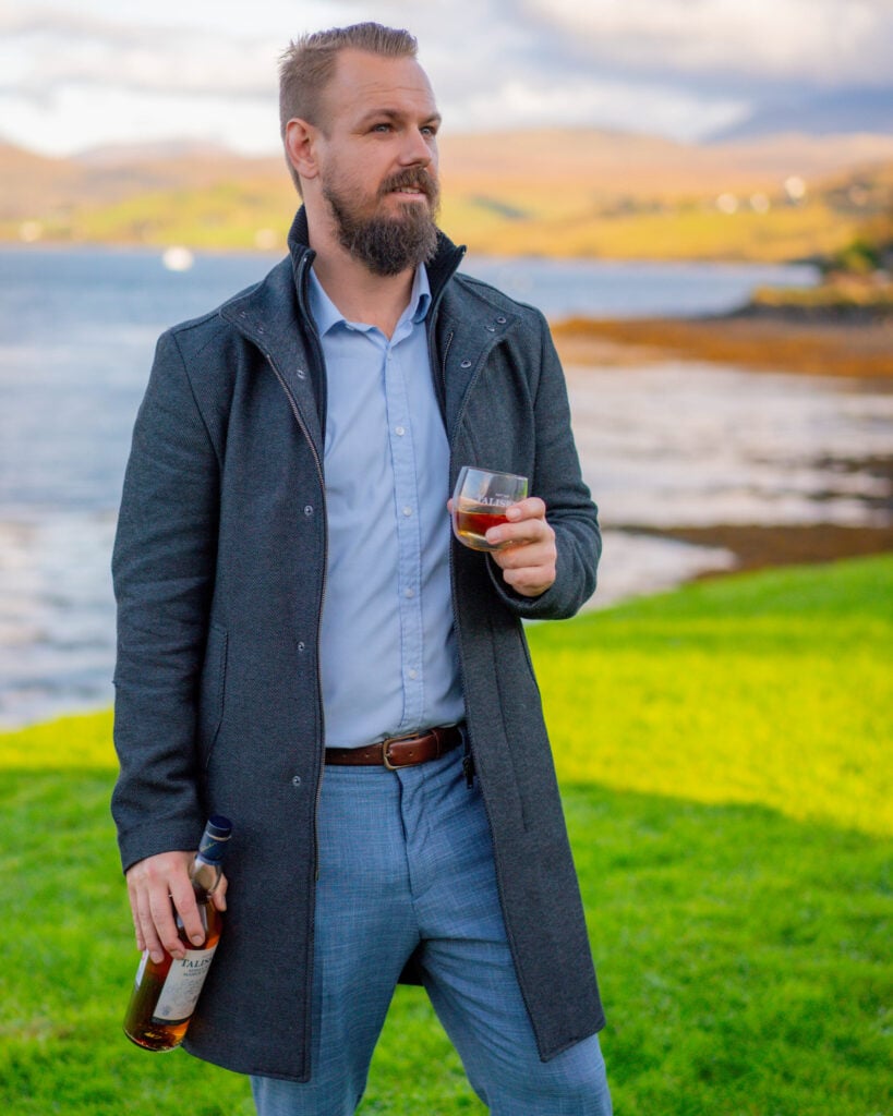 James Stevenson holding a whisky glass beside the water